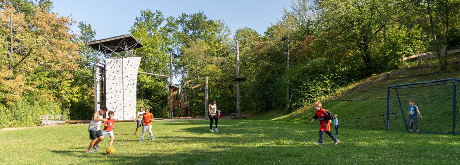 Kinder spielen Fußball, im Hintergrund steht ein Kletterturm
