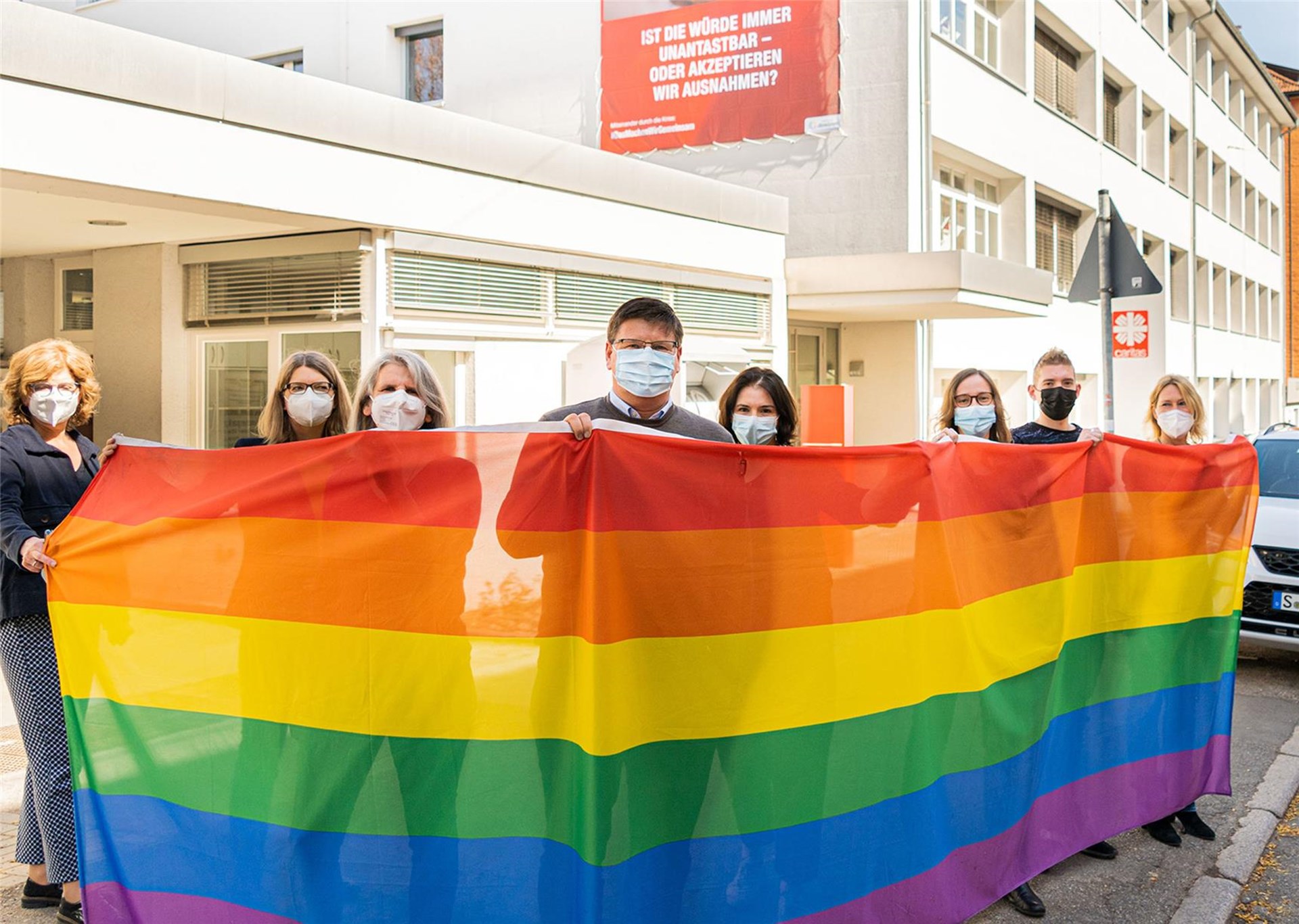 Caritas-Mitarbeitende halten eine Regenbogenfahne vor dem Haus der Caritas in Stuttgart-Ost.