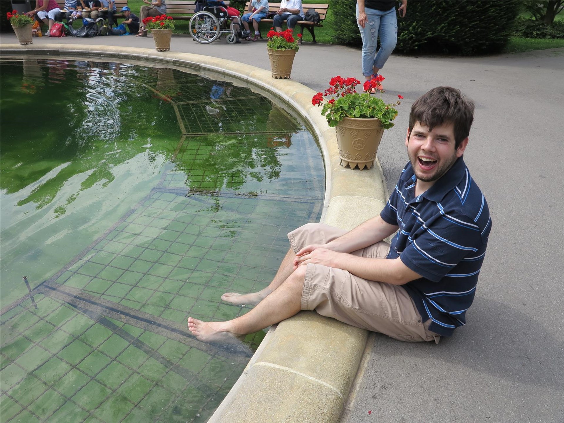 Ein junger Mann sitzt an einem Brunnen und hängt seine Füße ins Wasser